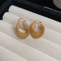 Détail de boucles d'oreilles créoles torsadées dorées avec finition texturée de luxe - Doré