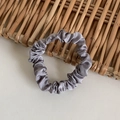 Silver grey satin scrunchie with elegant pleats displayed on a natural bamboo background - Gray