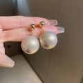 Primo piano di orecchini pendenti placcati oro con grandi perle bianche lucide - Perla Dorata (Perno in Argento)