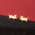 Primer plano de pendientes de gato dorado sobre una superficie de cuero negro texturizado - Dorado