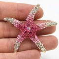 Dettaglio macro di una spilla a stella marina con strass rosa e pietra centrale iridescente - Bianco latte