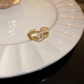 Detalle del anillo cruzado dorado con circonitas sobre un plato de cerámica blanca - Oro (7#)