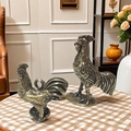 Dettaglio di figurine di gallo in ottone vintage con trama di piume su una tovaglia - Gallo Piccolo con Soldi