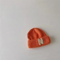 Detailed view of bright orange knitted beanie featuring a white plush N letter patch - Orange
