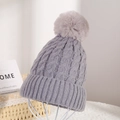 Detail of dark grey knit beanie with fluffy pompom on a white stand for winter - Gray