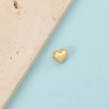 Detailed view of a golden heart-shaped bead with textured edges on a blue background - Gold