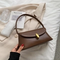 Retro brown faux leather underarm bag with gold oval buckle on beige blazer background - Caramel color
