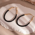 Detail view of large gold and black enamel oval drop earrings on a stone textured background - Gold + Black