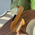 Détail d'une pince à cheveux en acétate ambré en forme de saxophone sur fond naturel - Saxophone Marron Doré