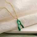 Close-up of golden box chain with green enamel abstract pendant on beige fabric - Letter A