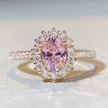 Macro shot of oval cut pink gemstone ring with diamond halo and rose gold band - US 5 / Padparadscha Pink - Rose Gold