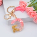 Detalle del llavero con letra G de resina rosa con copos dorados y borla decorativa - Letra G