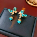 Dettaglio macro di orecchini a farfalla dorati con intarsio in turchese e pendente a perla - Blu Oro (Ago in Argento S925)