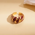 Macro detail of gold-tone geometric ring with deep red enamel stripes and textured surface - Burgundy