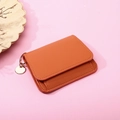 Detailaufnahme einer minimalistischen orangen Ledergeldbörse mit Ring auf rosa Grund - Orange