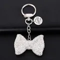 Detailed view of silver bowknot keychain with rhinestones and circular metal logo tag - White