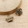 Macro detail of antique bronze crown charms on a rustic wood and fabric background - Antique Bronze