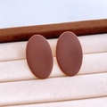 Makroansicht matter moccabrauner Oval-Ohrstecker mit Goldrand in einer beigen Schmuckbox - Braun