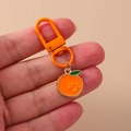 Detailed view of an orange-painted metal keychain featuring a cute cartoon orange pendant - Orange
