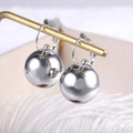 Close-up of polished silver sphere drop earrings hanging on a luxury display stand - White