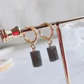 Detail of elegant gold hoop earrings with polished grey cylindrical natural stone pendants - Labradorite