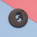 Detalle de un colgante redondo de metal negro con diseño calado de huella de bebé - 20mm / Negro