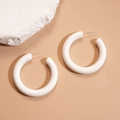 Detailed view of minimalist white acrylic C-shaped earrings on a beige textured background - White