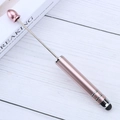 Rose gold metallic eye massage roller wand on white wooden desk for beauty care - Pink
