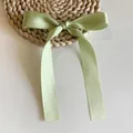 Detail of sage green satin ribbon bow hair clip with long streamers on a woven mat - Duckbill Hair Clips / Short/PC / Fruit Green