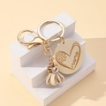 Close-up of golden keychain with MAMA engraved wooden tag and leather tassel on white steps - Off White