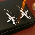 Macro shot of silver iris flower earrings on a black reflective jewelry box surface - Silver