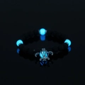 Luminous turtle bracelet with black volcanic stone beads glowing blue on reflective surface - Turtle + Sky Blue Luminous