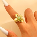 Detailed close-up of a golden four-petal flower ring with a green bead on a finger - Gold (3851)