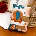 Short beige fabric wallet featuring colorful elephant patterns and brown leather strap closure - Handheld Elephant Pattern