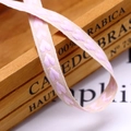 Macro detail of beige cotton ribbon featuring pink heart embroidery for gift wrapping - 10mm / Pink