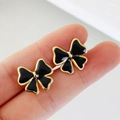 Elegantes pendientes de lazo negro y dorado en acero inoxidable mostrados en las yemas - Negro