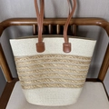 Two-tone woven straw tote bag featuring brown leather handles on a wooden chair - Wheat Beige