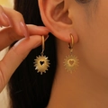 Close-up of golden sunburst hoop earrings with heart cutout worn by a model - Stainless Steel / Hollow Sun Heart - Gold