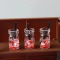 Macro detail of three miniature strawberry resin drink bottles with tiny black straws - Fruit Cup 11