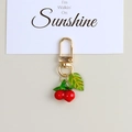 Close-up of vibrant red resin cherry keychain with green leaf and golden D-ring buckle - Cherry Shape Pendant