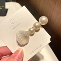 Detail view of a shell hair clip with white pearls and gold metal on a display card - 8* Beaded Large Shell - White