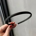 Minimalist black satin headband with a smooth finish held by a hand for size scale - Black