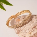 Detail eines zweireihigen Strass-Goldarmbands auf Naturstein mit grünen Blättern verziert - Doppelarmreif / Gold