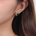 Close-up of heart-shaped gold earrings with emerald green crystals worn by a model - Green