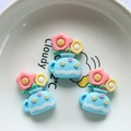 Detail view of three blue resin teapot charms with colorful flowers in a white bowl - Vase