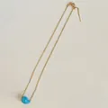 Detail of gold chain necklace featuring a glossy sky blue bean pendant and lobster clasp - Universal Chain / Blue