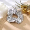 Chic silver metallic scrunchie hair tie on a beige textured tray with lifestyle decor - Silver
