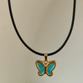 Detailed view of 18k gold plated butterfly pendant with blue enamel on a black cord - Blue