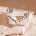 Close-up of a silver polished wide cuff bracelet with wavy edges on a stone surface - Silver Twisted Wave Streamline Style