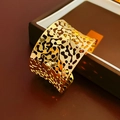 Détail macro du bracelet manchette doré ajouré posé sur un coffret cadeau de luxe - Doré